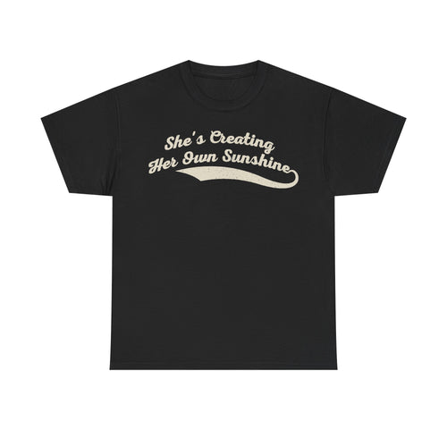 T-shirt in black with beige vintage script text She's Creating Her Own Sunshine across the chest.