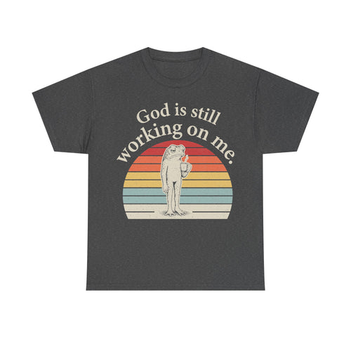 T-shirt in dark charcoal with vintage sunset circle and frog graphic; God is still working on me.