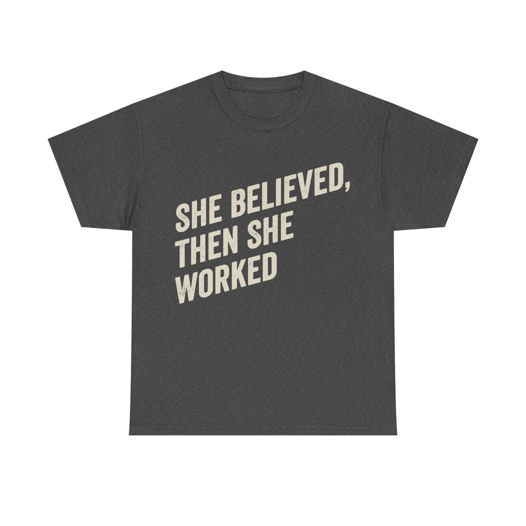 Charcoal gray T-shirt with bold cream text reading SHE BELIEVED, THEN SHE WORKED.